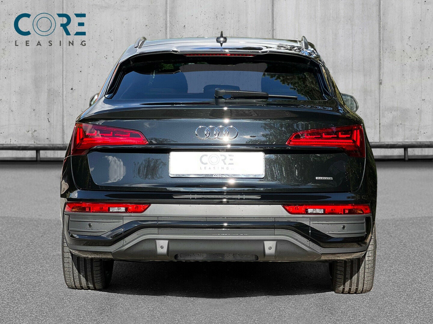 Sortmetal Audi Q5 TFSi e S-line Sportback quattro S-tr. fra 2021 parkeret foran en betonmur. CORE Leasing A/S er eksperter i Audi leasing.